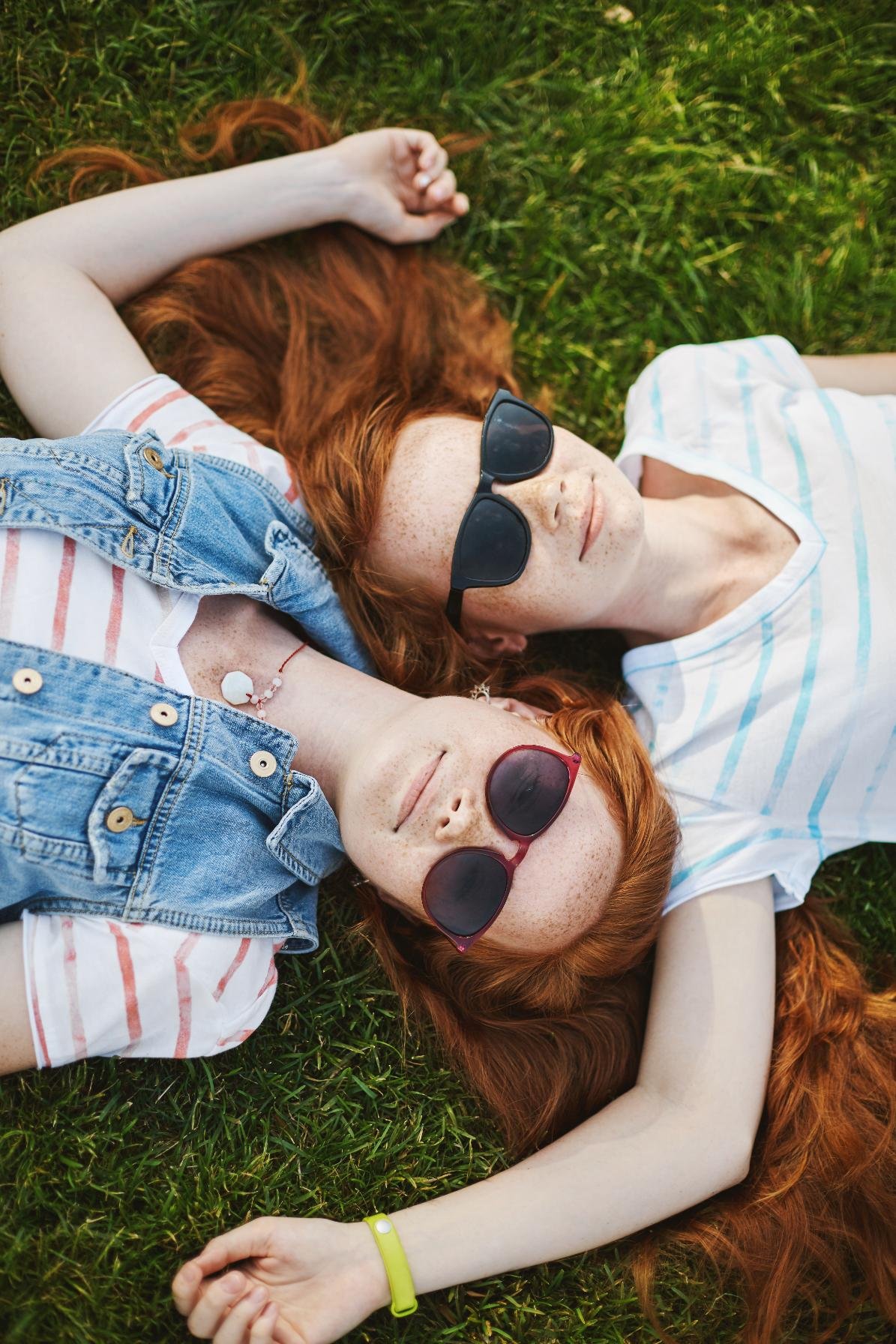 vertical-shot-beautiful-relaxed-happy-girls-with-natural-ginger-hair-cute-freckles-lying-grass-touching-each-other-heads-wearing-cool-sunglasses-chilling-sun-warm-summer-day